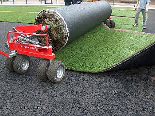 Kunstrasen wird auf der Elastikschicht positioniert, ausgerollt und justiert